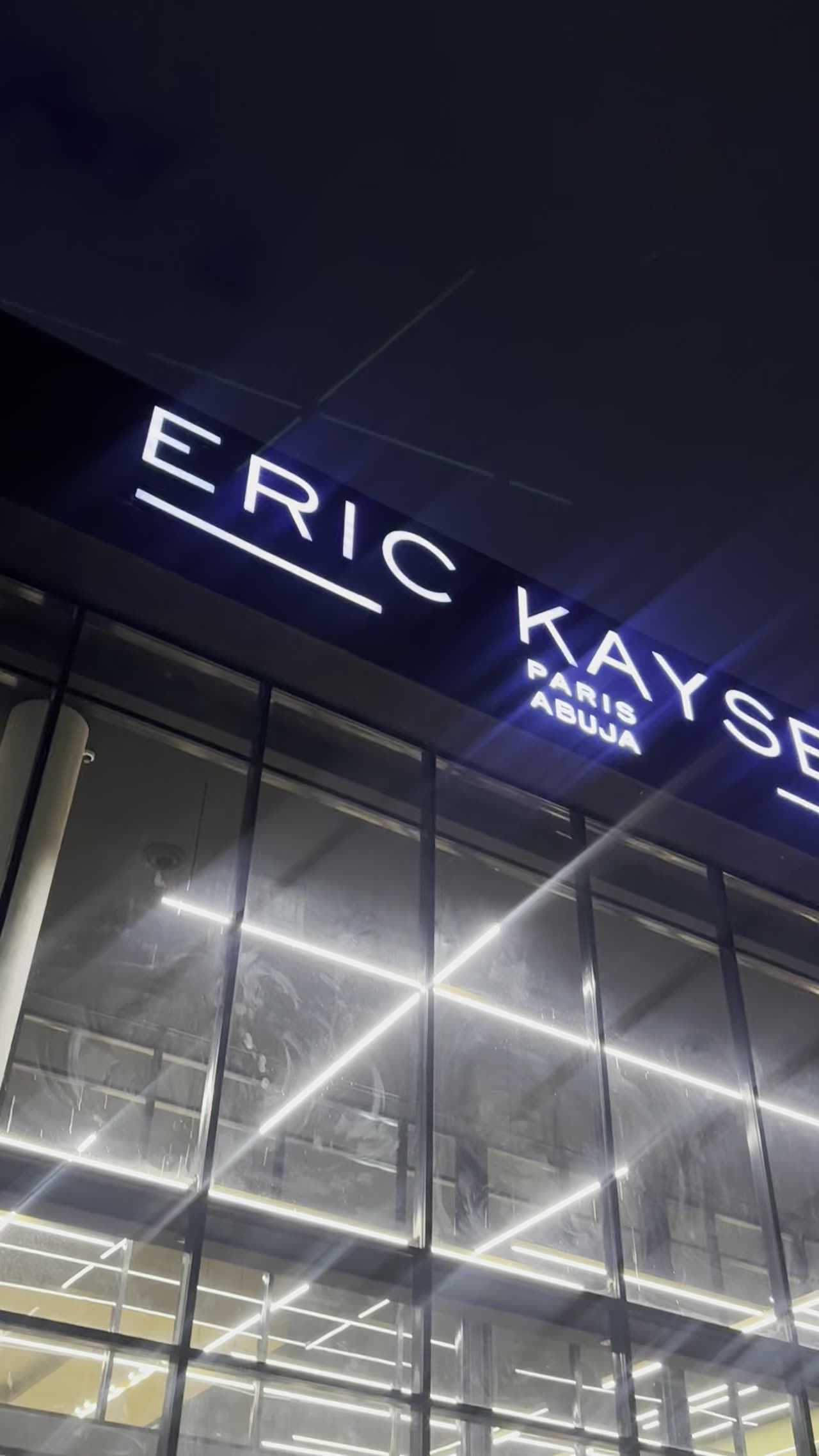 The Eric Kayser Abuja signage lit against the night sky, the glass floor glowing behind it